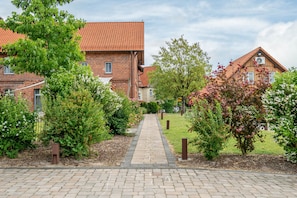 Un bâtiment en briques surmonté d’un toit en tuiles, avec un chemin pavé et de la verdure tout autour.