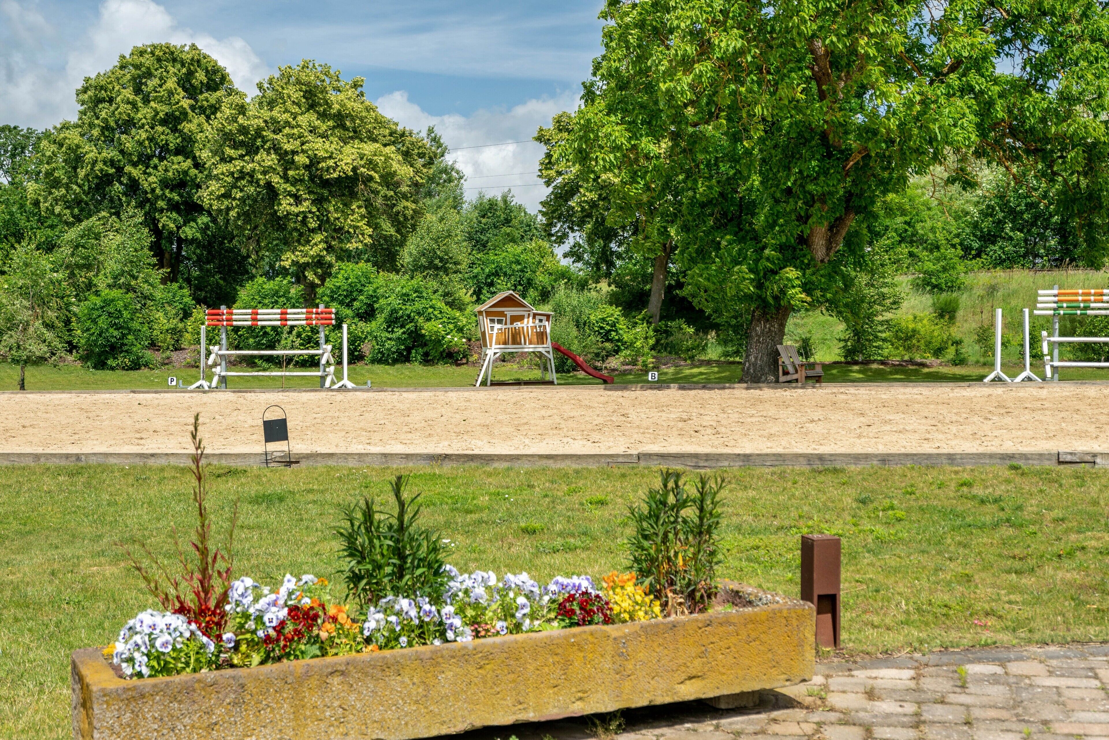 A park with a wooden play structure, a sandpit, and a flower bed.