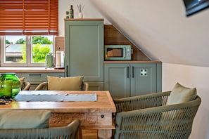 Una cocina acogedora con comedor, un armario verde, un microondas y una ventana con persianas.