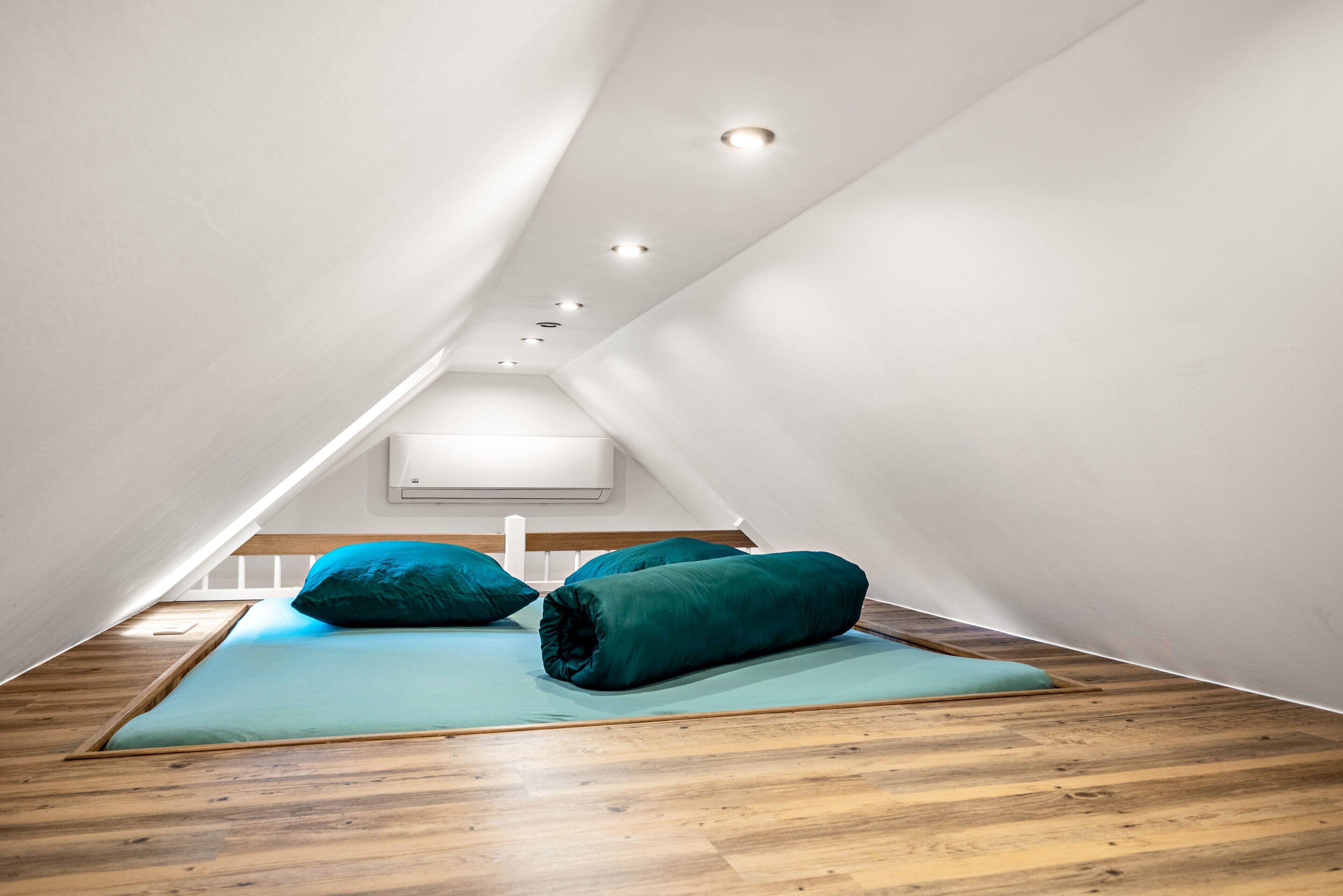 A modern, minimalist room with a sloped ceiling, wooden flooring, and a bed with teal bedding.