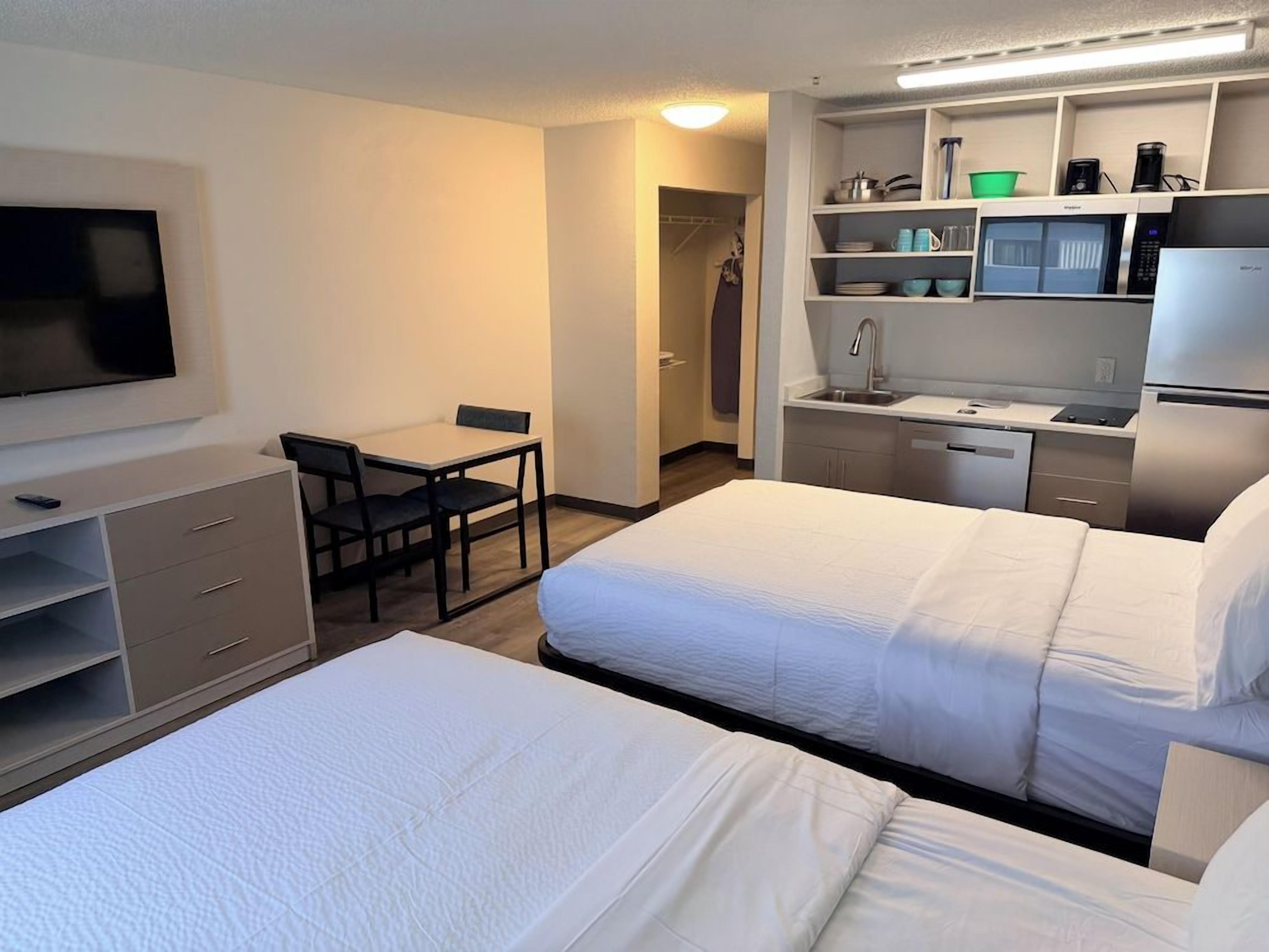 A hotel room with two beds, a desk, a chair, a television, and a kitchenette with a microwave, coffee maker, and sink.