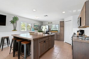 Una cocina con una isla grande, taburetes de bar, un refrigerador y un fregadero.