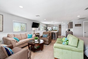 A spacious living room with a sofa, armchairs, a coffee table, and a kitchen area in the background.