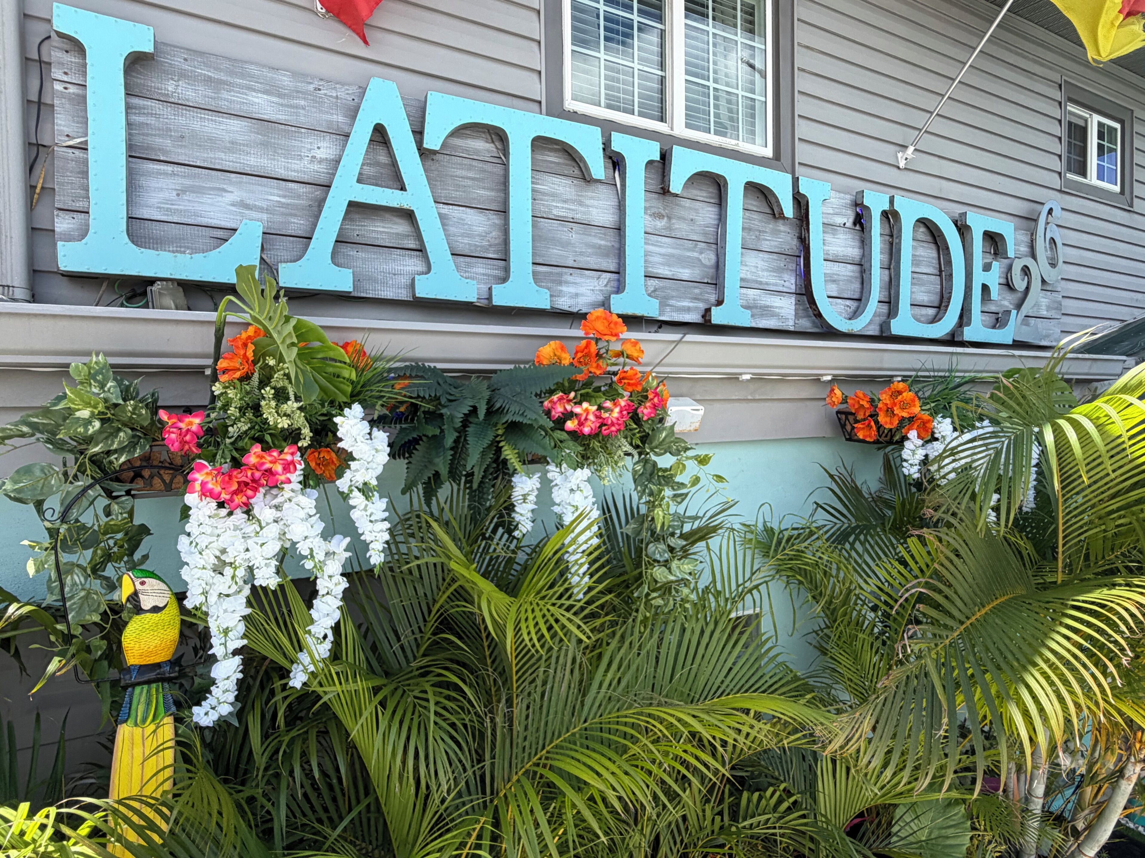 Un bâtiment sur lequel on peut lire l’inscription « LATITUDE », et qui est entouré de différentes plantes et fleurs.