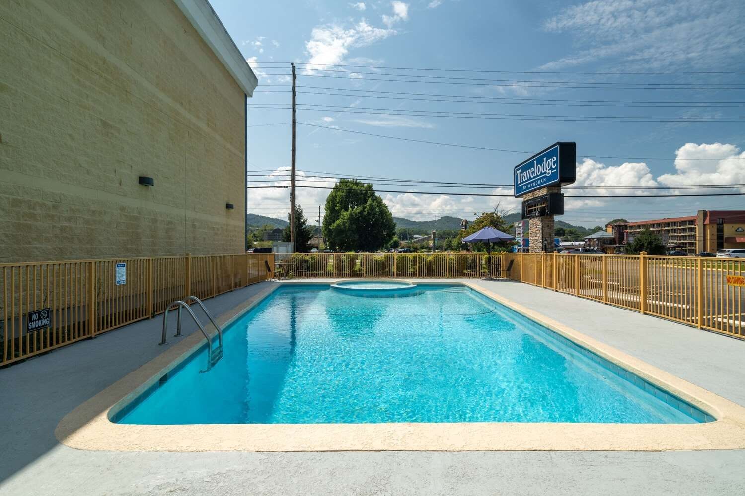 Une piscine avec un panneau indiquant qu’il est interdit de fumer, un panneau indiquant la présence d’un hôtel Travelodge et une zone délimitée par une clôture.