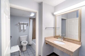 A bathroom with a toilet, a shower, a sink with a mirror, and a towel rack. - Travelodge By Wyndham Pigeon Forge (Pigeon Forge)