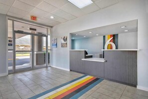 A reception area with a glass door entrance, a reception desk, and a large number '6' sign on the wall. - Studio6 Rosenberg, TX (Rosenberg)