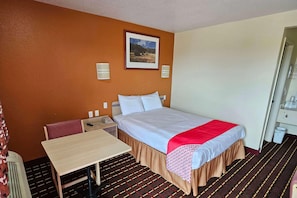 Une chambre d’hôtel comprenant un lit, une table, une chaise, une table de chevet, un téléphone et un tableau encadré au mur.