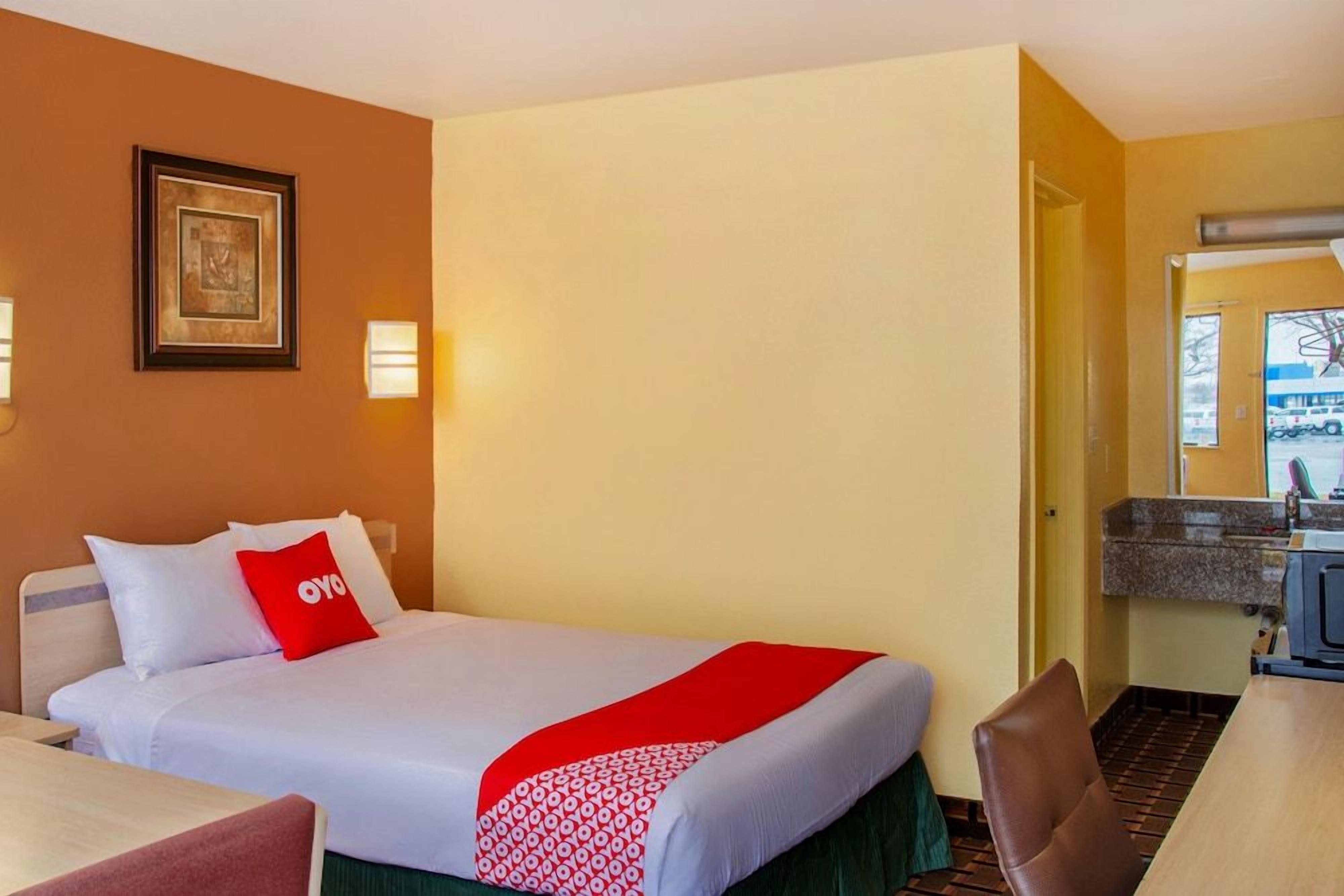 A hotel room with a bed, a desk, a chair, a framed picture on the wall, and a door leading to a bathroom.