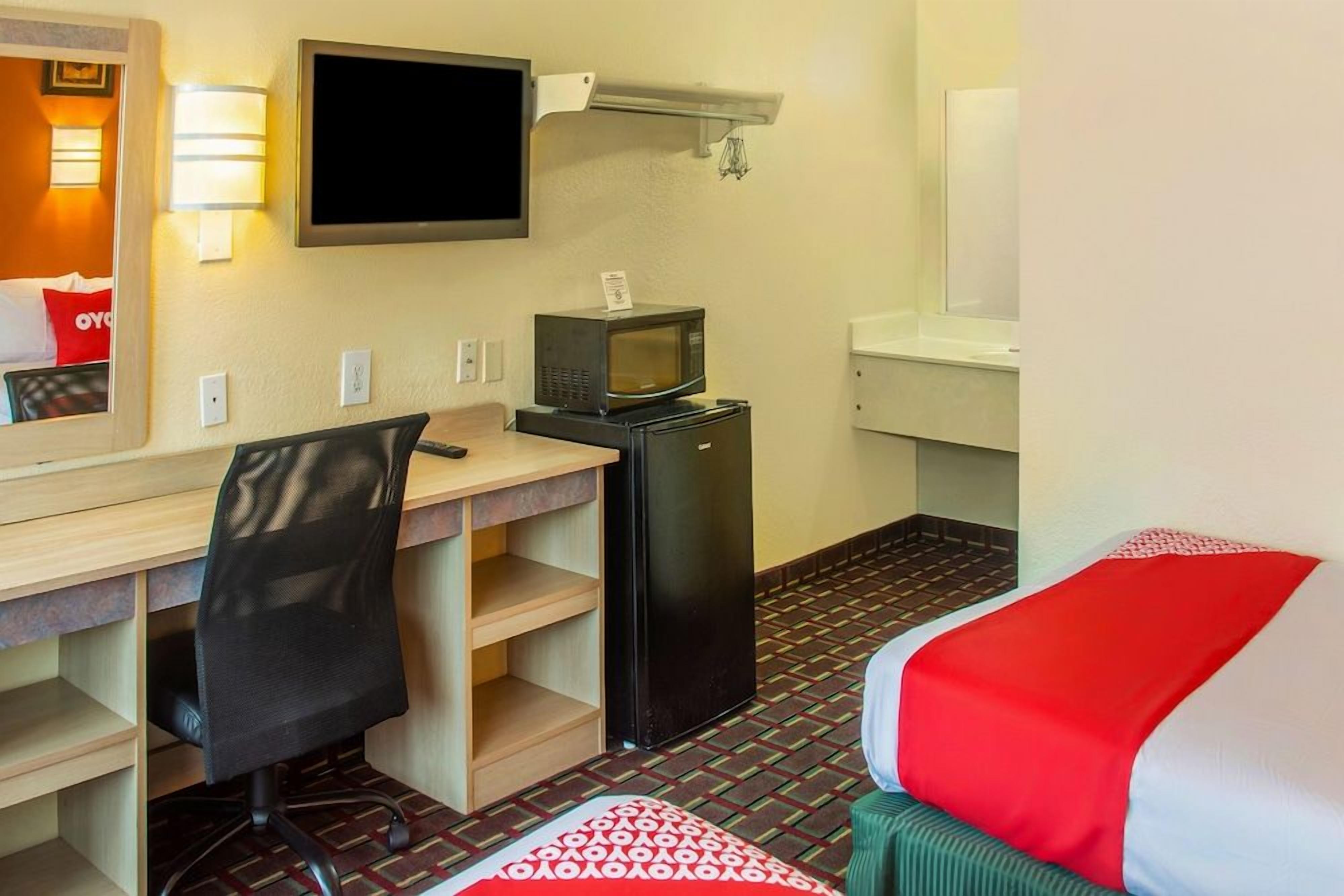 A hotel room with a desk, chair, bed, TV, microwave, and refrigerator.