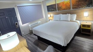 A hotel room with a bed, bedside tables, a desk, a chair, and a large window with a view. - Days Inn by Wyndham Wichita Falls (Wichita Falls)