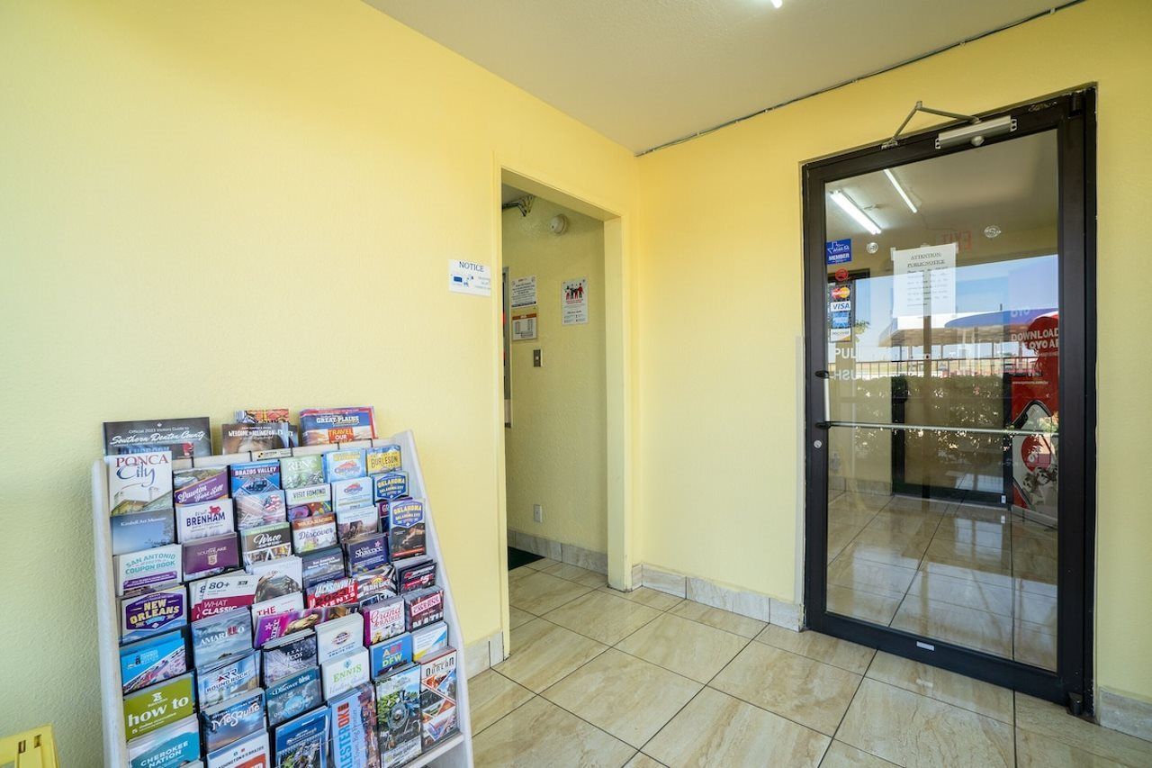 A hallway with a glass door leading to a room, a bulletin board with various flyers, and a tiled floor.
