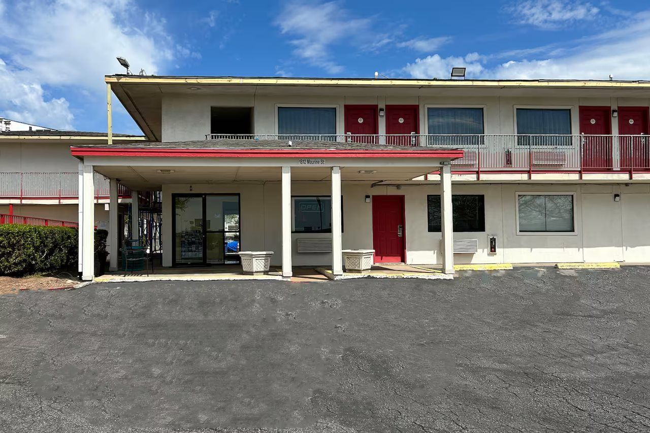 A motel with a covered parking area, a single-story structure, and a red and white color scheme.