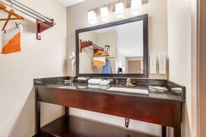 A bathroom with a dark wooden vanity, a large mirror, and a towel rack. - Econo Lodge Childress, TX (Childress)