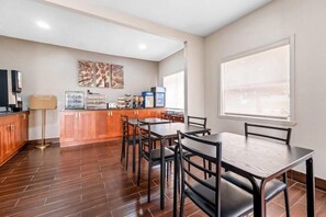 A modern kitchen with wooden cabinets, a dining area with a table and chairs, and artwork on the walls. - Econo Lodge Childress, TX (Childress)