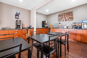 Une cuisine d’hôtel avec un espace repas, des machines à café et un téléviseur.