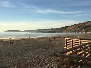 A beach with a wooden walkway, pebbles, and distant hills. - Motel6 Pismo Beach, CA - Pacific Ocean (Pismo Beach)