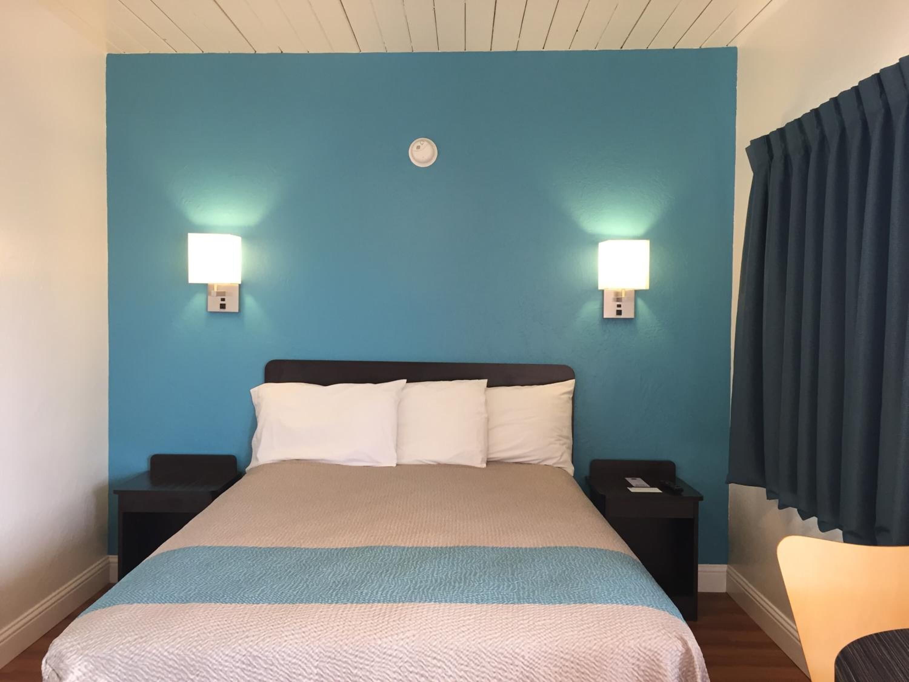 Quarto de hotel com uma cama grande, duas mesas de cabeceira, um criado-mudo, uma cadeira e uma janela com cortinas.