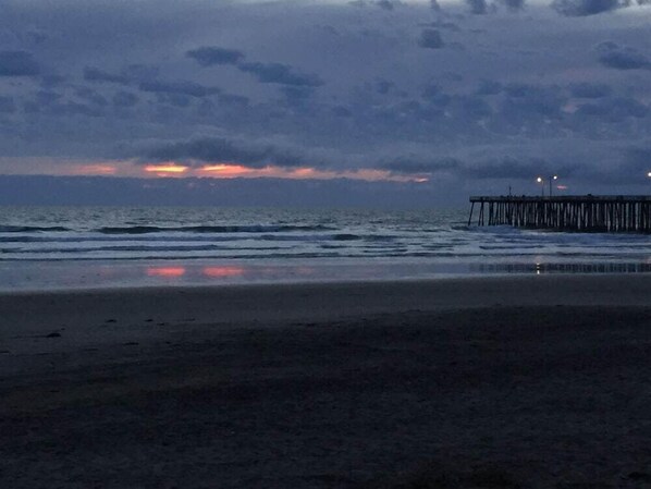 A beach with a wooden pier extending into the water, waves gently lapping at the shore, and a sunset in the background. - Motel6 Pismo Beach, CA - Pacific Ocean (Pismo Beach)