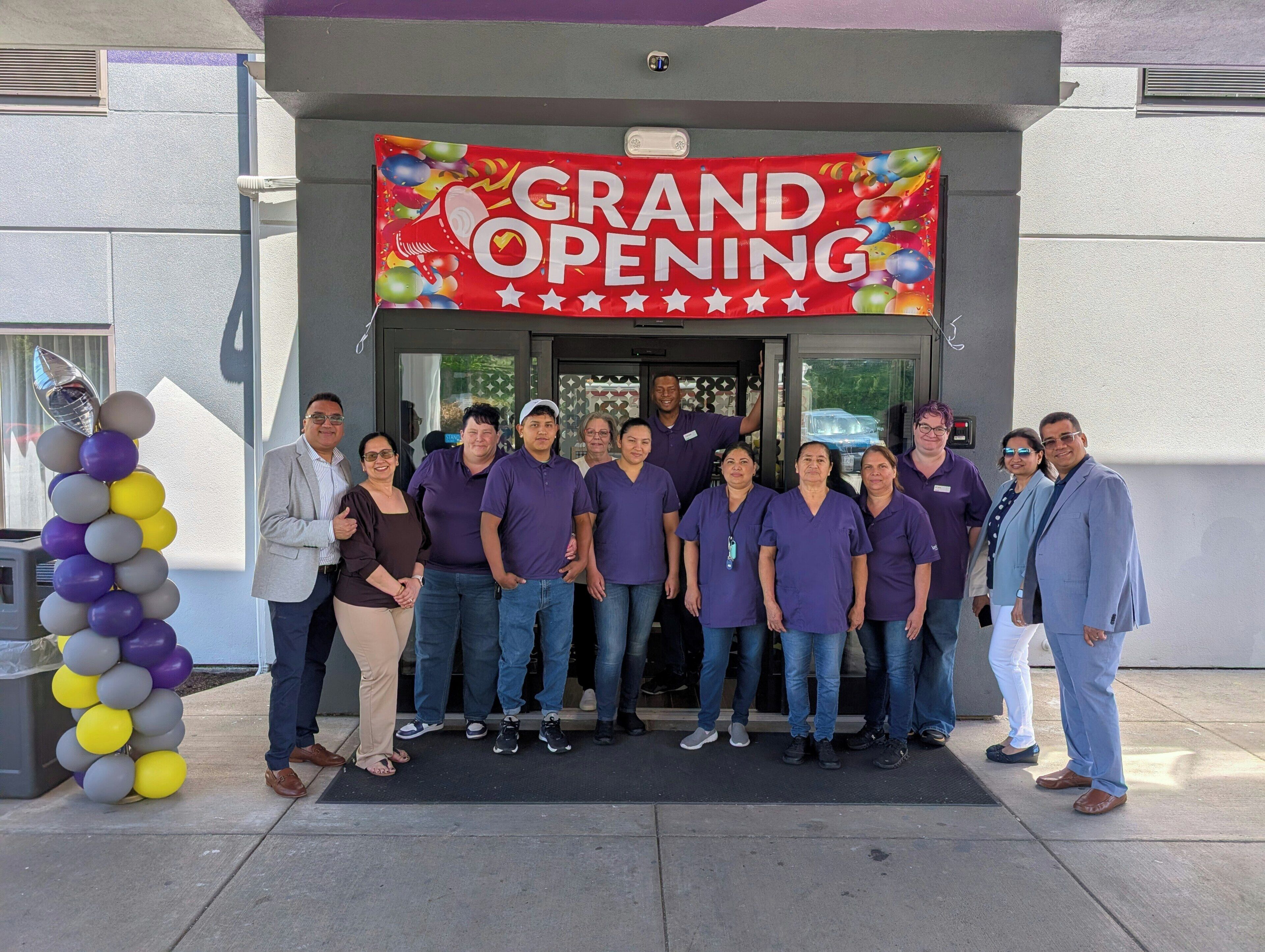 A group of people in front of a building with a 'GRAND OPENING' sign.