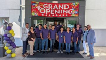 A group of people in front of a building with a 'GRAND OPENING' sign.