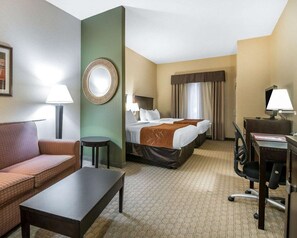 Een hotelkamer met een bank, een bed, een bureau, een stoel, een lamp en een spiegel.
