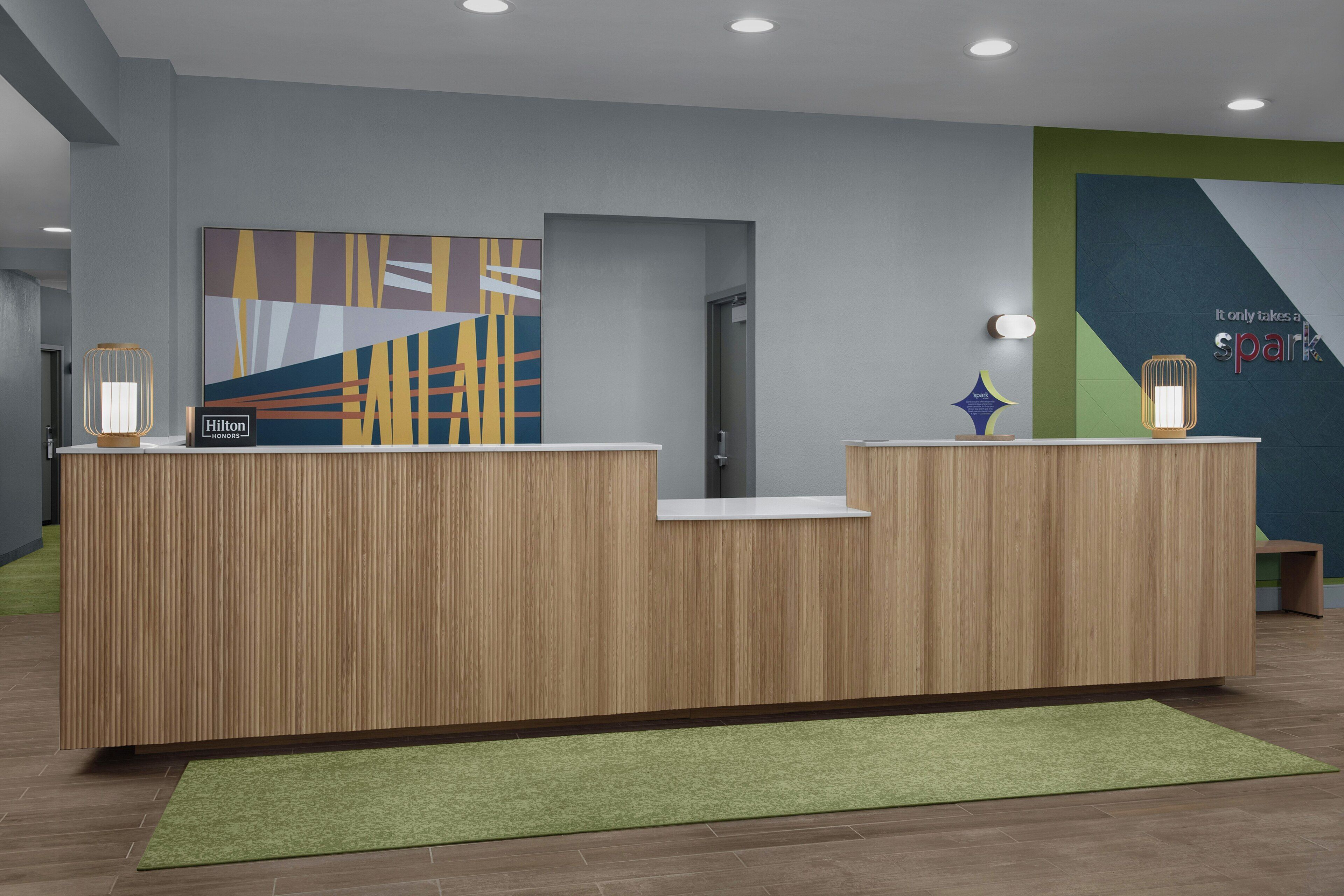 A reception desk with a modern design, a green carpet, and a wall with a geometric pattern.