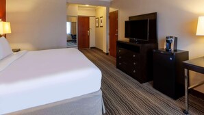 A hotel room with a bed, a television, a dresser, and a desk.