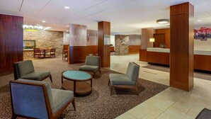 A lobby with a reception desk, seating area with chairs and a round table, and a stone wall.