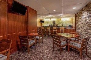A hotel bar with wooden furniture, a flat-screen TV, and a stone wall. - Trademark Collection by Wyndham Liverpool/syracuse (Liverpool)