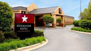 A hotel entrance with a sign, a flag, and a clear sky. - Magnuson Hotel Bourbonnais (Bourbonnais)