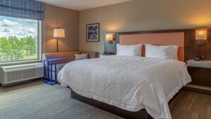 A hotel room with a large bed, a desk, a chair, a window with a view, and two wall-mounted lamps. - Magnuson Hotel Bourbonnais (Bourbonnais)