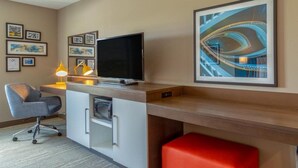 A modern hotel room with a desk, chair, television, artwork, and a red ottoman. - Magnuson Hotel Bourbonnais (Bourbonnais)