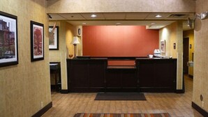 A hotel reception area with a reception desk, framed pictures on the walls, a clock, and a carpeted floor. - Magnuson Hotel Bourbonnais (Bourbonnais)