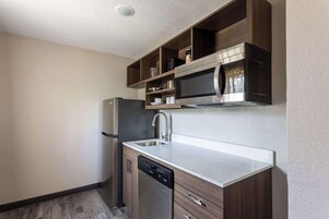 A compact kitchen with a built-in dishwasher, a stainless steel refrigerator, and a microwave above the countertop.