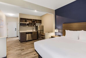 Ein Hotelzimmer mit Bett, Schreibtisch, Küchenzeile und Badezimmer.