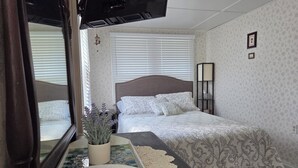 Un dormitorio con cama, una mesita de noche con una planta, un espejo y una ventana con persianas.