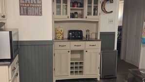 Una cocina con suelo de madera, armarios blancos y un microondas.