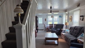 Un salón espacioso con escaleras, ventilador de techo, zona de comedor y vistas al exterior.