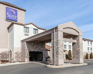 A Sleep Inn & Suites building with a stone facade, a covered entrance, and a clear sky. - Inn & Suites Near I-90 And Ashtabula (Austinburg)