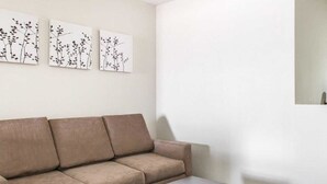 Un salon aux couleurs neutres, avec un canapé et une table basse, et trois œuvres d’art accrochées au mur représentant des motifs végétaux abstraits.