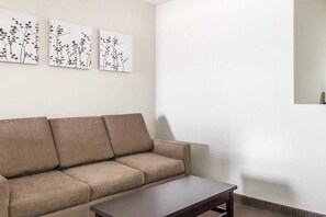 Un salón comedor en tonos neutros con sofá y una mesa de centro, y tres obras de arte colgadas en la pared que representan diseños abstractos de plantas.