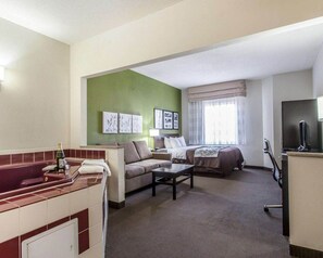 Quarto de hotel com cama, sofá, mesa pequena, televisão e banheiro com banheira e pia.