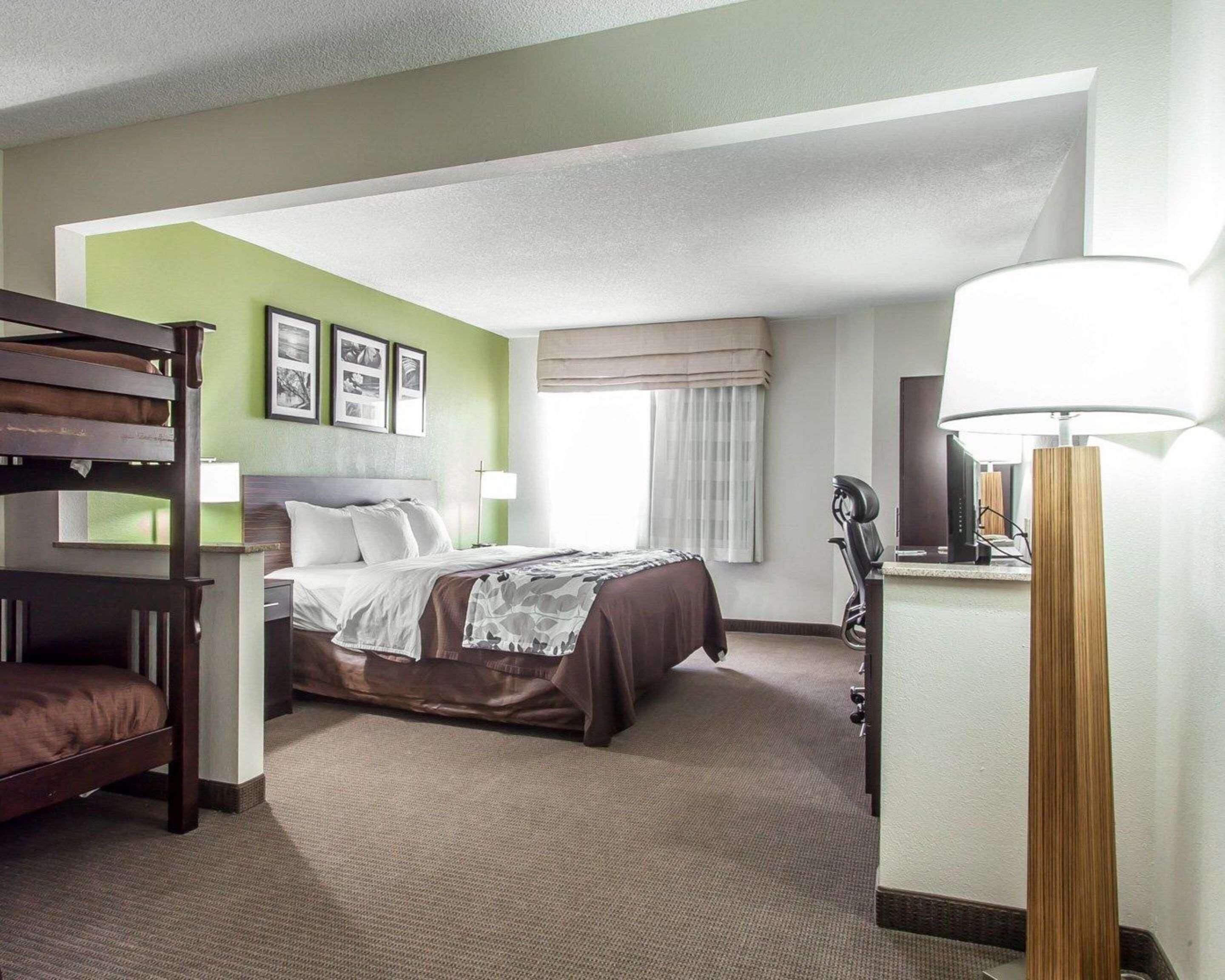 A hotel room with a bed, a desk, a chair, a lamp, and a bunk bed.