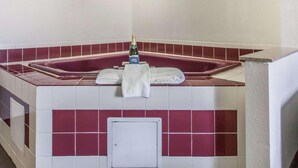 Une salle de bain avec une baignoire carrelée de carreaux rouges et blancs, deux appliques murales et une bouteille de champagne posée sur le bord de la baignoire.
