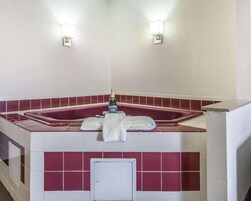 Un baño con una bañera de azulejos rojos y blancos, dos luces empotradas en la pared y una botella de champán sobre el borde de la bañera.