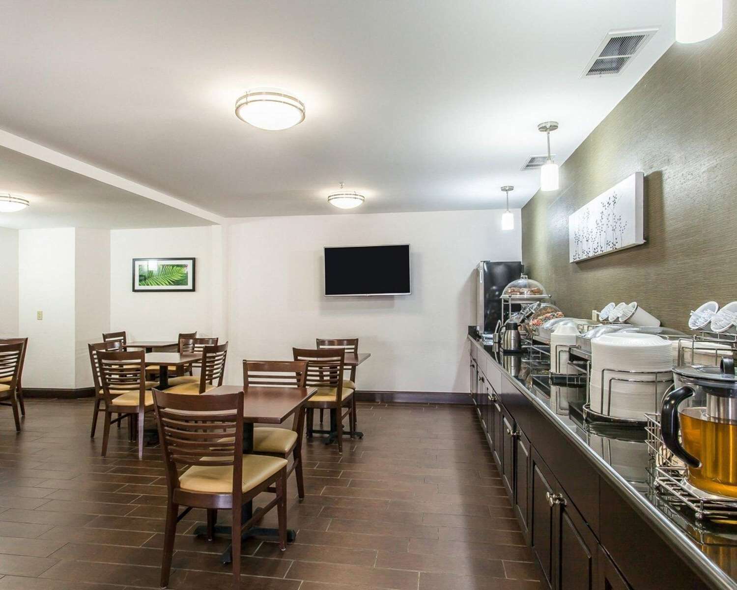 A dining area with tables and chairs, a flat-screen TV mounted on the wall, and a buffet counter with various food items and a coffee machine.