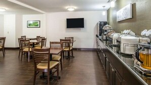 Un espace repas avec des tables et des chaises, un téléviseur à écran plat fixé au mur, et un buffet proposant divers plats et une machine à café.