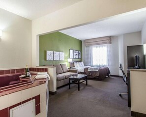 Habitación de hotel con cama, sofá, escritorio, televisor y baño con bañera.