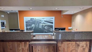 Vastaanottotiski, jossa on suuri näyttö, jolla esitetään mainos, ohjauspaneeli ja puulattia.